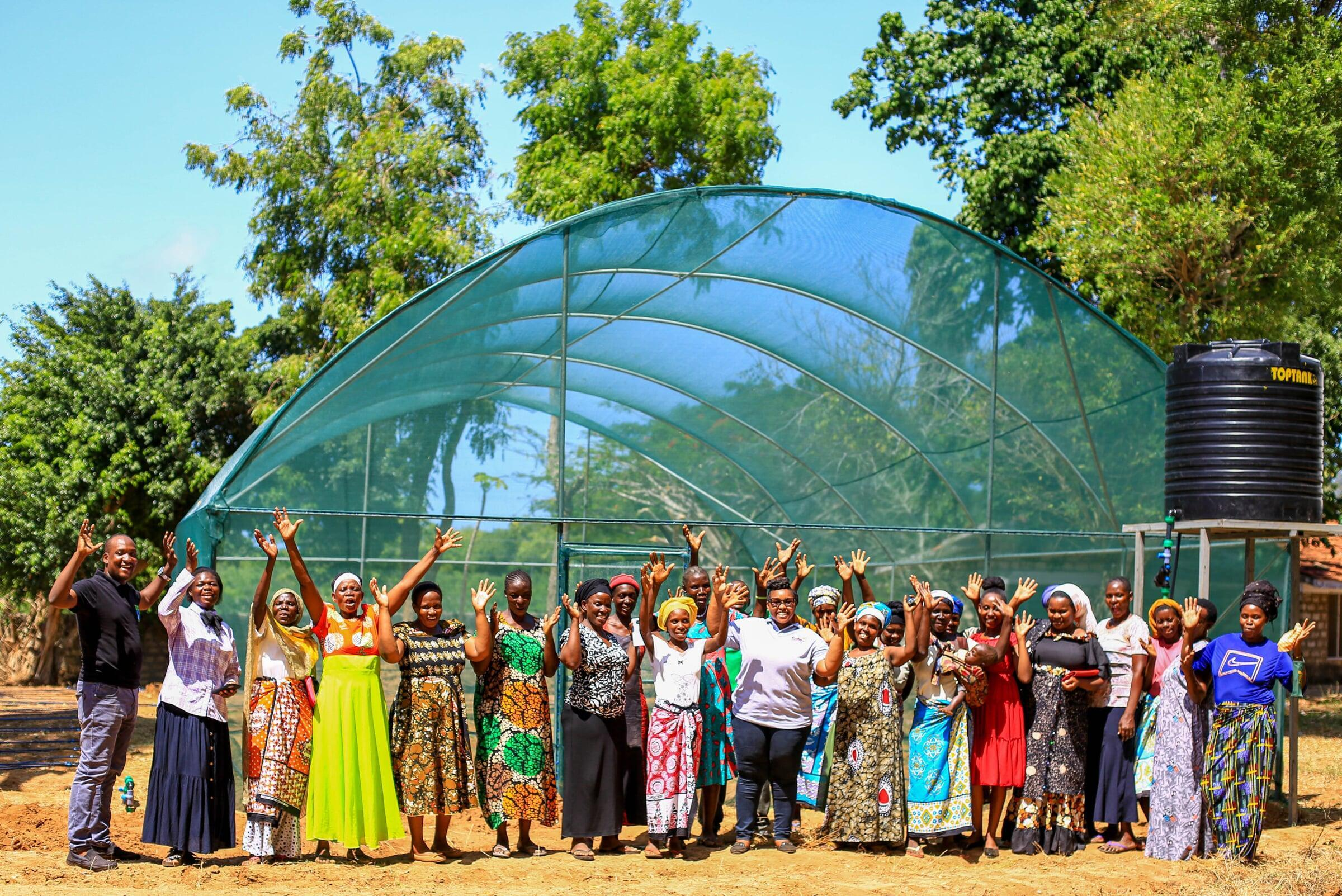 Community members celebrating together in front of a newly built greenhouse and water tank